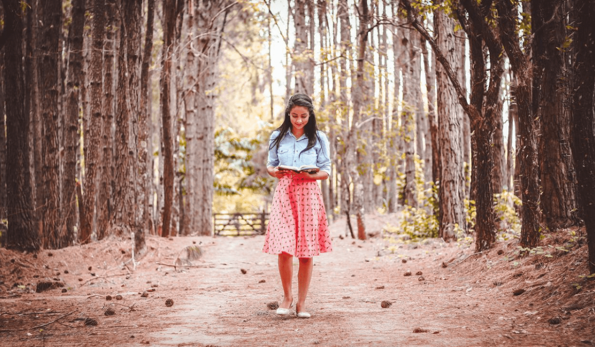 Una mujer lee un libro mientras camina por un sendero forestal